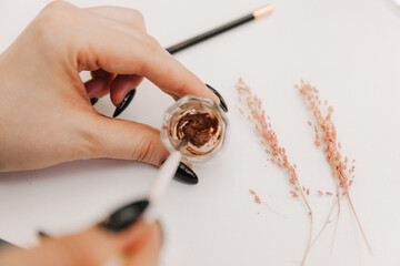 close-up of the master's hands holding a brush with which he stirs the eyebrow paint in a cup