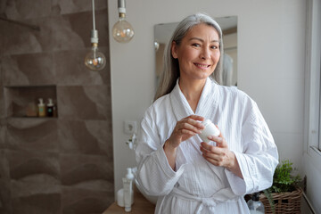 Pretty Asian woman holding cosmetic jar in the bathroom