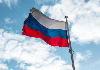 Russian flag or flag of Russian Federation waving on flagpole against blue sky