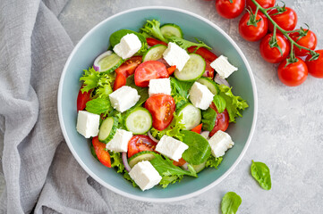 Salad with fresh vegetables and cheese in a bowl on a concrete background. Greek salad, vegetarian dish. Top view.