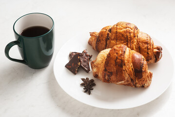 delicious, crispy croissants, chocolate, hot coffee in the blue cup and kitchen towel on plate on marble table