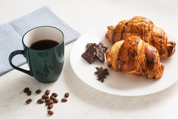 delicious, crispy croissants, chocolate, hot coffee in the blue cup and kitchen towel on plate on marble table