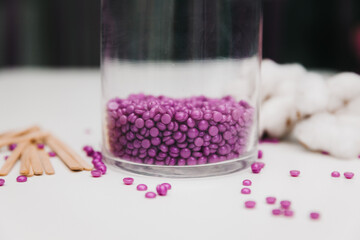 Close-up of purple wax granules scattered from a jar. Beauty procedure to remove unwanted hair from...