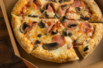freshly baked pizza with mushrooms and ham in a cardboard box on a wooden table