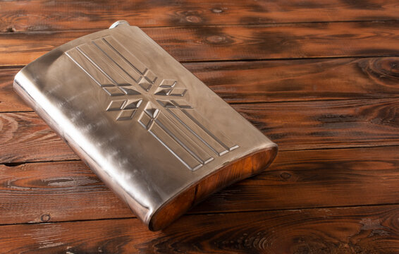 a metal flask for alcoholic beverage is on wooden background.