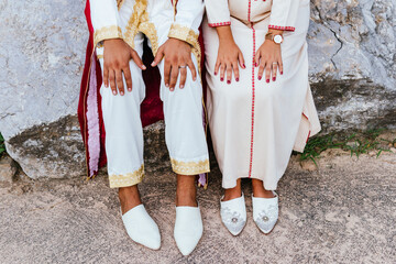 shot of the hands and shoes of an arabian couple dressed with traditional clothes sitting on a stone.