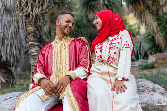 low angle image of a charming arab couple dressed with traditional clothes sitting on a stone and looking each other