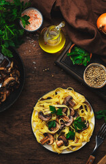 Tasty fettuccine pasta with mushrooms served on plate with greens and spice on rustic wooden kitchen table background, top view. Healthy vegetarian cooking and eating. Italian food concept