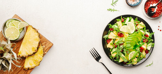 Vegan vegetarian salad with pineapple, arugula, avocado and dried cherry on white stone kitchen table, top view. Healthy eating, clean diet food, weight loss concept