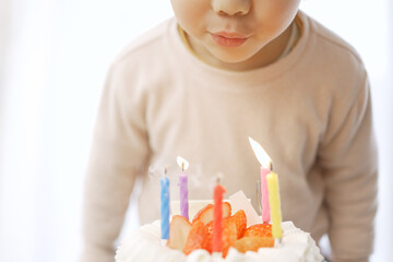 誕生日ケーキのロウソクの火を吹き消すアジア人の男の子	