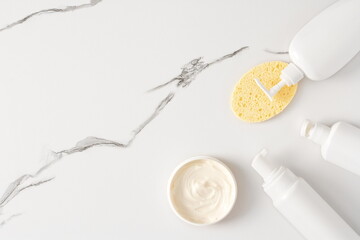 Foaming facial cleanser open bottle with foam sample and face cleansing sponge on marble background. Top view, flat lay. Copy space