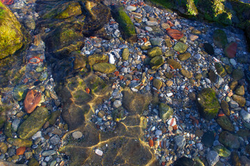 Fototapeta na wymiar Rocky bottom of a beach with crystal clear waters and stones of different colors 