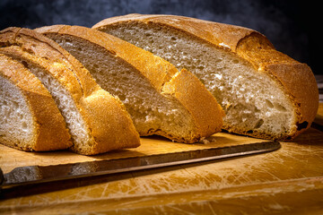 slice loaf of traditional rustic village bread cut into slices with knife on a wooden board