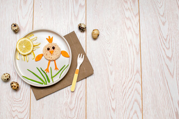 Obraz na płótnie Canvas Easter funny creative healthy breakfast lunch food idea for kids, children. chicken shape sandwich from bread, peeled carrots, greens vegetables on plate wooden table background. Top view Flat lay