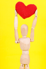 wooden man with a red heart in his hands on a yellow background