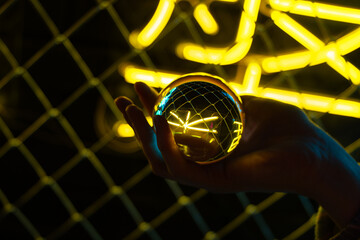 A hand holds a shining ball with a reflection of neon lights. Storyteller of the future. The...