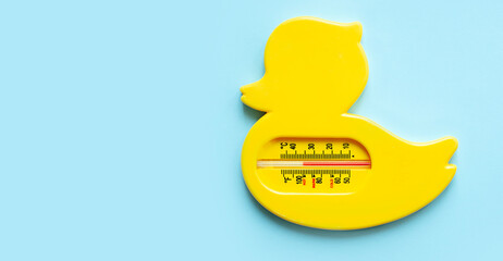 Children's bathing thermometer on a blue background. Yellow duck thermometer for measuring water temperature. Baby care. Banner.Top view.Copy space.