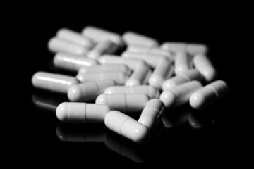 Close up of white painkiller capsule on a reflective black background