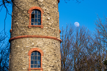 windows in an old round brick tower in front of full moon in blue sky
