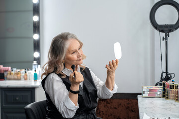 Beautiful elderly woman looks in the mirror in a beauty salon