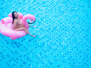 Chubby happy young woman dressed in swimsuit with inflatable flamingo in blue swimming pool.