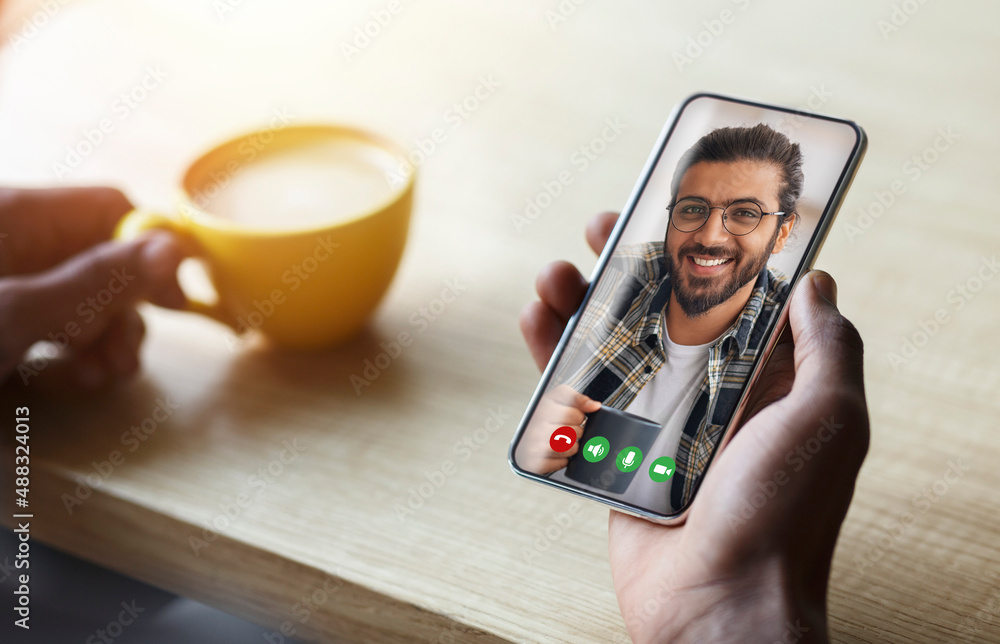 Poster man using smartphone in cafe for video call with middle eastern friend