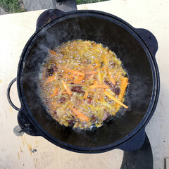 Cauldron with cooked pilaf. Cooking plov at home, a step-by-step recipe for real pilaf. A piece of meat, carrot, rice in boiling oil. Traditional oriental pilaf on a sunny day, close-up.