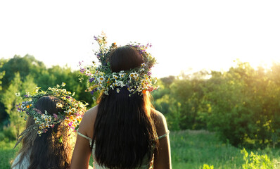 Two girls in flower wreaths on meadow, sunny green natural background. Floral crown, symbol of...