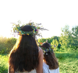 Two girls in flower wreaths on meadow, sunny green natural background. Floral crown, symbol of...