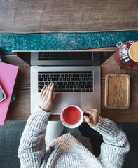 Woman working on a laptop in a cafe with a cup of tea, top view.