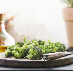 Close up of broccoli roses at wooden cutting board with kitchen knife at background with natural light and cooking utensils. Healthy cooking at home with green vegetables. Front view.