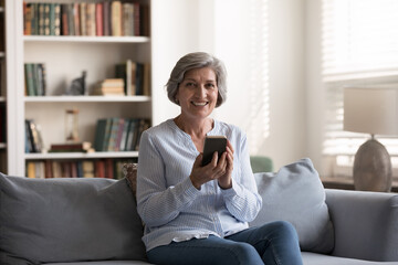 Obraz premium Portrait of smiling beautiful mature old woman holding cellphone in hands, enjoying web surfing information, communicating or shopping online, playing games, modern tech gadgets addiction concept.
