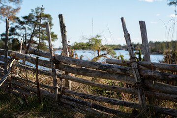 Fototapeta na wymiar Traditional old wooden roundpole fence on the countryside. Idyllic view of the countryside and landscape with the water and forest in the background. Photo taken in Oskarshamn, Sweden.