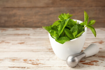 Mortar with mint leaves and pestle on table