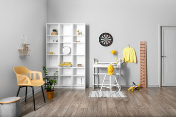 Interior of light children's room with workplace, shelving unit and dartboard