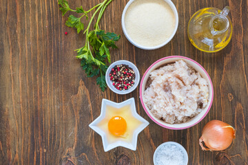 Ingredients for cooking fish cakes on a wooden background: minced fish, egg, spices, onion, breadcrumbs. Recipes fish, seafood.