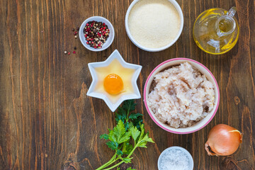 Ingredients for cooking fish cakes on a wooden background: minced fish, egg, spices, onion, breadcrumbs. Recipes fish, seafood.