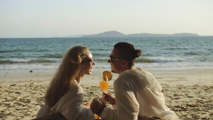 Carefree loving couple in white dress, sunglasses, relax and drinking cocktail Pina Colada, pineapple slice. Concept sea beach resting tropical tourism, summer holidays, food beverage alcohol