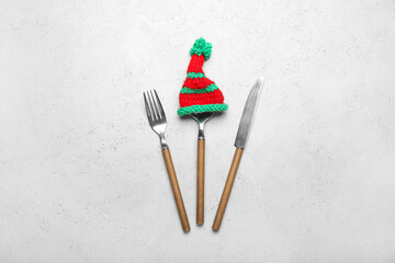 Set of cutlery with wooden handles and knitted hat on light background