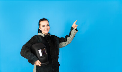 a happy brunette girl dressed in a protective welding suit and mask points to the text. space for text. men's professions