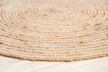 Stylish wicker rug on light wooden floor, closeup