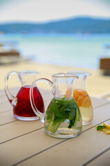 Refreshing cold drinks with various herbs and fruits in jugs on the table on the beach