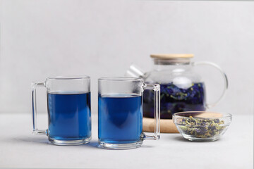 Two cups of fresh organic blue anchang tea in clear glass cups on a gray table. Herbal Thai tea. Selective focus.