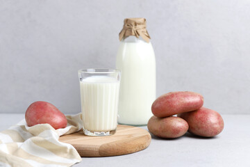 Vegan plant milk in a glass glass and bottle. Alternative potato milk and potato tubers on a gray background. Selective focus.