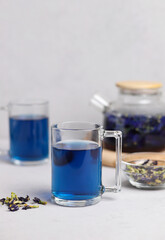 Organic fresh blue anchan tea in a transparent glass cup on a gray table. Herbal Thai tea. Selective focus. Vertical photo.