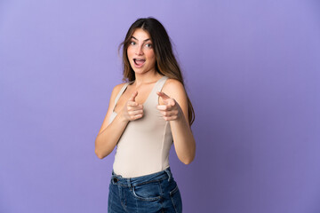 Young caucasian woman isolated on purple background surprised and pointing front