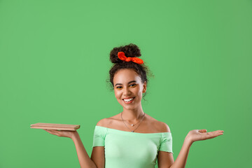 Beautiful young African-American woman with book on green background