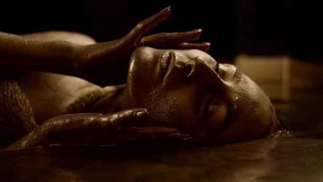Close-up portrait of a mysterious woman lying in golden water as in a dream.