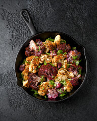 Roasted purple, white cauliflower with herbs on cast iron pan