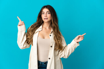 Young caucasian woman isolated on blue background pointing finger to the laterals and happy